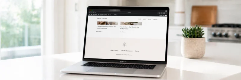Laptop on a bright white kitchen island displaying a WordPress blog footer in browser preview with Privacy Policy, Affiliate Disclosure and Terms links visible as part of a guide to GDPR for bloggers