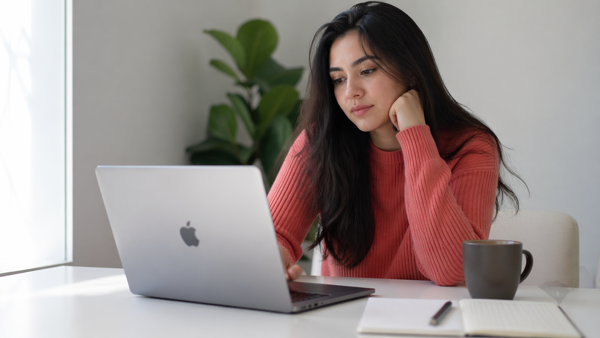 Woman at a desk using a laptop with a notebook and coffee while working on Pinterest for blogging