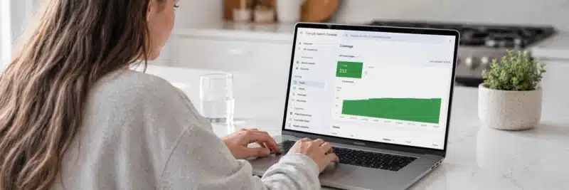Laptop on a bright white kitchen island displaying the Google Search Console coverage report with a growing number of valid indexed pages showing the results of fast indexing WordPress setup