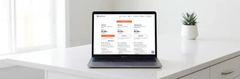 Laptop on a bright white kitchen island displaying the Hostinger hosting plan pricing comparison page showing Premium Business and Cloud Startup options as part of a Hostinger pros and cons review