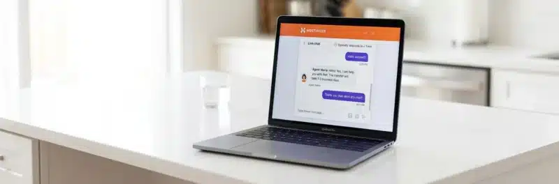 Laptop on a bright white kitchen island displaying the Hostinger live chat support window with an active conversation showing responsive customer support